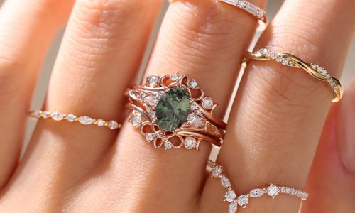 A hand wearing a green sapphire ring with an enhancer ring and 4 stacking rings.